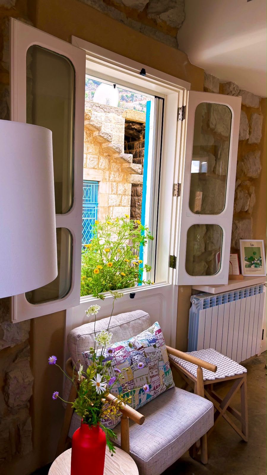 Open traditional shutters framing wildflowers and the stone facades of Douma's souk