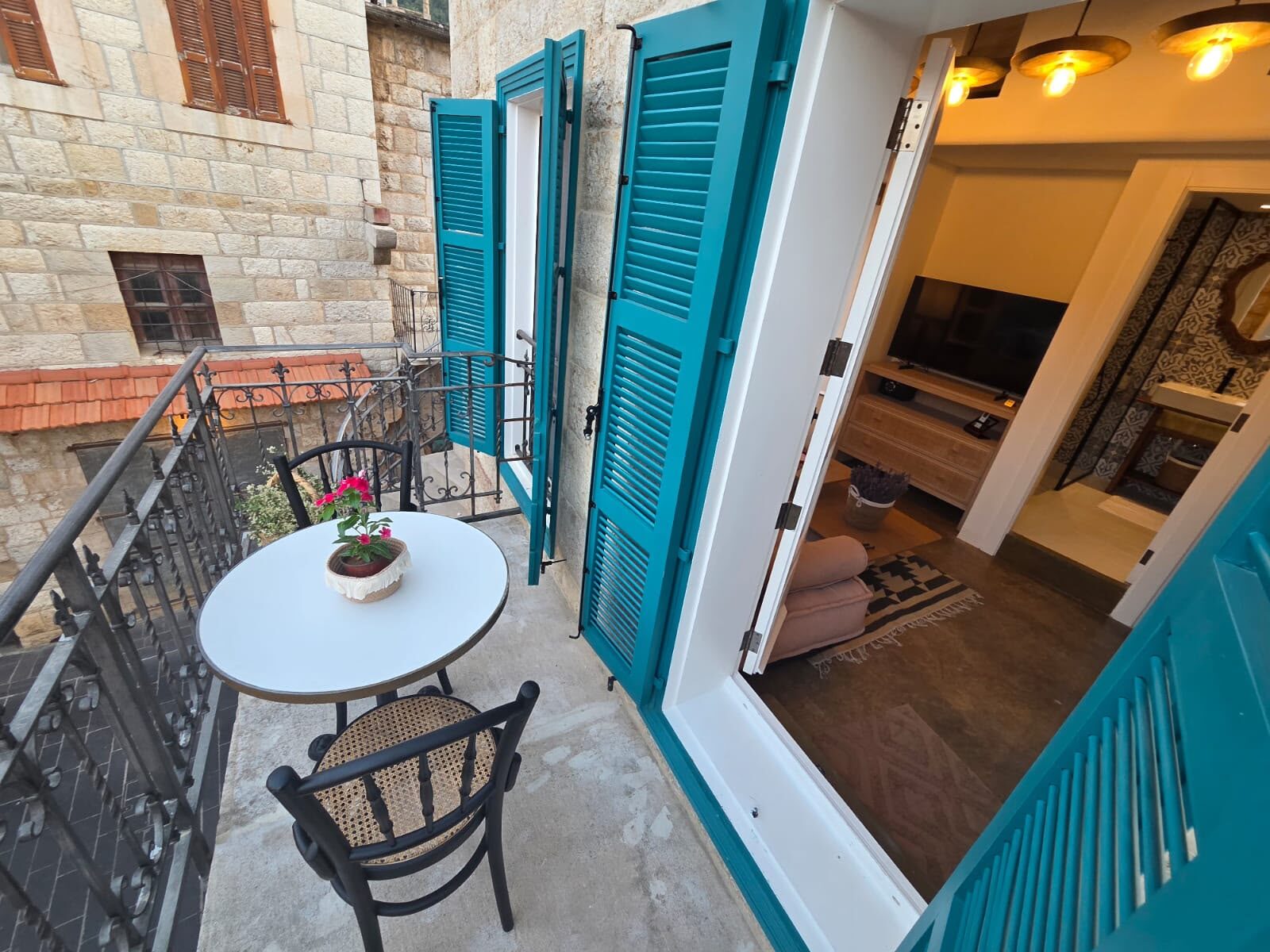 Tale balcony with teal shutters, a bistro table and a view over the souk's stone alley