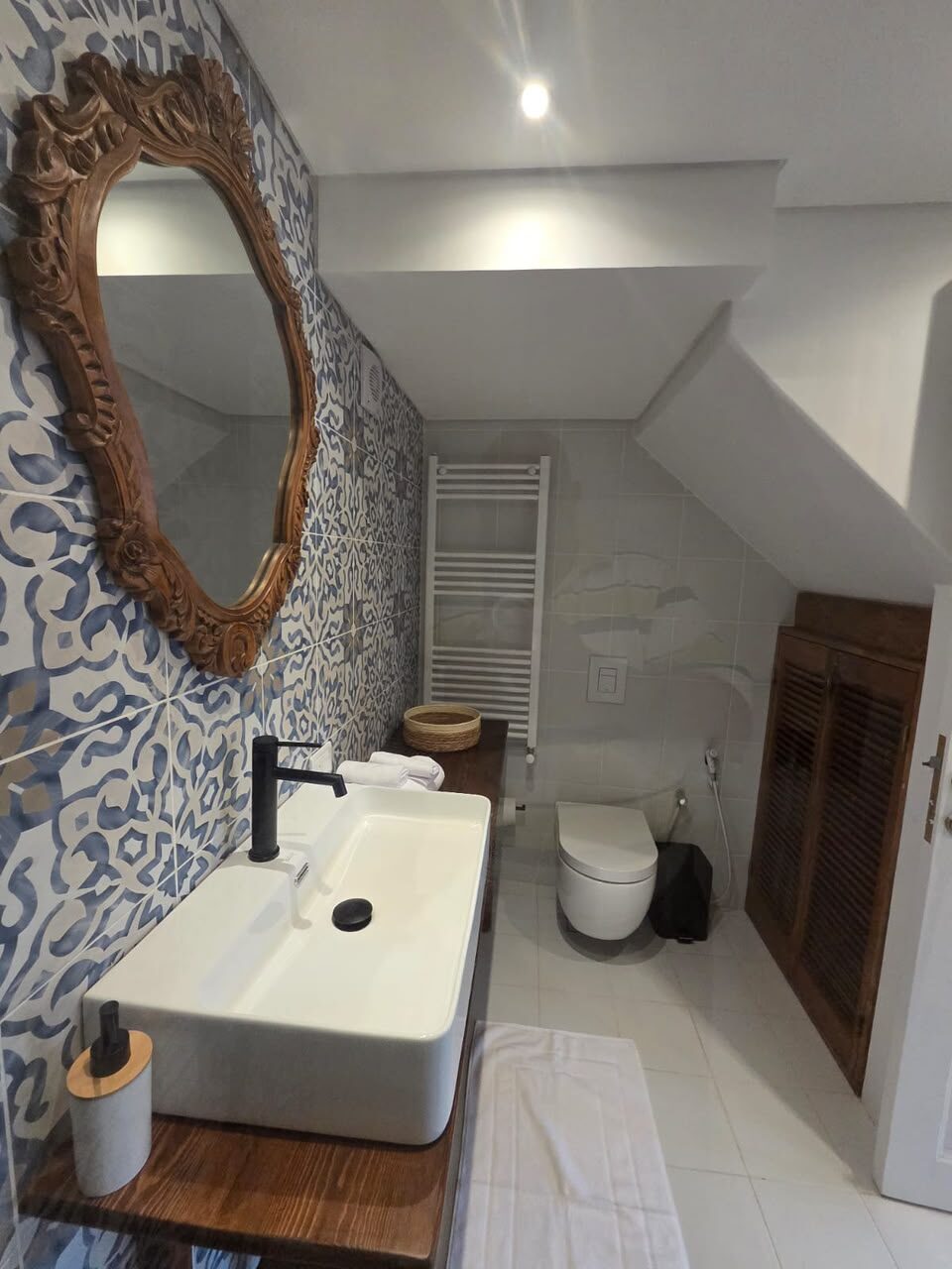 Tale en-suite bathroom with blue patterned tiles, a carved mirror and a white vessel basin