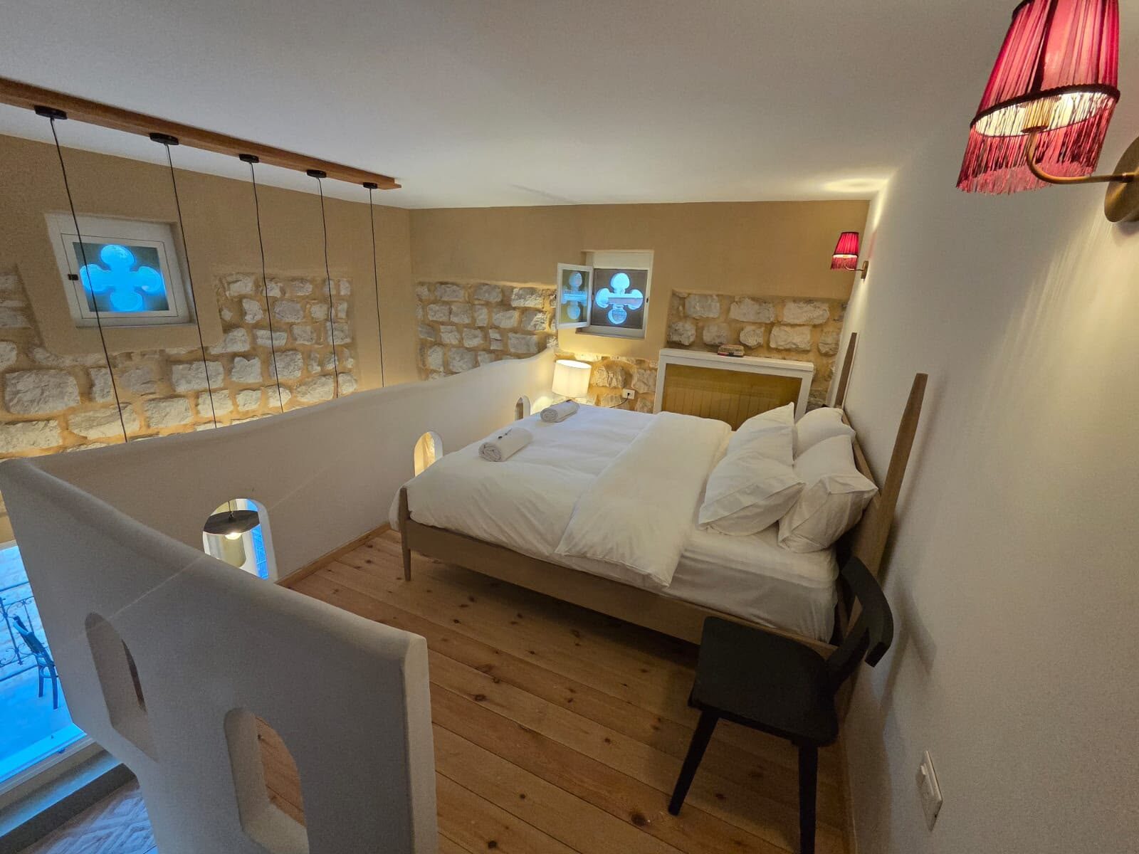 Tale bedroom with a made bed, whitewashed walls and a red glass pendant lamp
