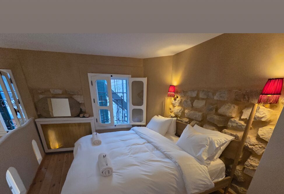 Whisper bedroom with a made bed, red wall lamps and a bare stone headboard wall